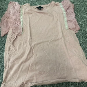 Rosa topp från Amisu med spetsdetaljer - Säljer en söt rosa topp från Amisu med volangärmar och spetsdetaljer längs axlarna. Perfekt för en romantisk look. Toppen är i ett mjukt material och har en avslappnad passform. Mer rosa i verkligheten 