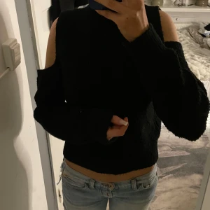 Svart stickad tröja från Gina Tricot - Säljer en svart stickad tröja från Gina Tricot. Tröjan har en unik design med en ärmlös och en lång ärm, vilket ger en cool asymmetrisk look. Perfekt för att lägga till en edgy touch till din outfit.