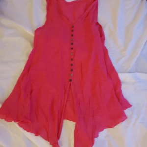 Rosa ärmlös topp med knappar - Säljer en söt rosa ärmlös toppen med knappar framtill. Den har en luftig passform och volangdetaljer vid fållen. Perfekt för varma dagar!