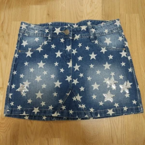 Vintage Jeanskjol - Snygg blå jeanskjol från OVS med ett coolt stjärnmönster på fram och baksida. Kjolen har praktiska fickor både fram och bak samt en knapp i midjan. Perfekt för en trendig look!