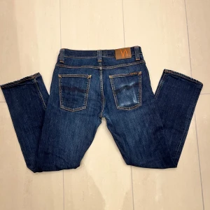Mörkblå jeans från Nudie Jeans - Riktigt snygga mörkblå jeans från Nudie Jeans som visar på en stilren look. Jeansen har använts sparsamt men ändå fått den här mer vintage utseendet som visar tecken på att den åldras väl. Perfekta för en dag i skolan eller till en utekväll med kompisarna🤙🤩W33 L32.