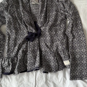 Marinblå mönstrad kofta från Odd Molly - Säljer en snygg mönstrad kofta från Odd Molly i storlek 1. Koftan har ett unikt mönster i marinblått och vitt och är tillverkad i 100% bomull. Den har långa ärmar och en knytning framtill som ger en fin detalj. Perfekt för att ge din outfit en extra touch!