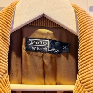Beige vintage manchesterkavaj. Polo Ralph Lauren - Säljer en snygg beige manchesterkavaj från Polo Ralph Lauren. Kavajen har en klassisk design med knappar framtill och fickor. Perfekt för en stilren look. Passar bra till både vardag och mer formella tillfällen. Nypris 5700kr