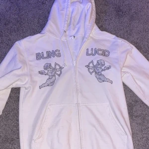 Vit zip  hoodie med bling detaljer  - Säljer en vit hoodie från Bling Lucid. Hoodie har jag innehavt i cirka 8 månader. Köptes för 1000kr. Priset går såklart ner mer för hålet som finns i den. Det är däremot enkelt att sy igen för den kunniga 