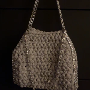 Grå stickad handväska - Snygg grå stickad handväska med coola kedjehandtag. Perfekt för att ge din outfit en unik touch. Väskan har en rymlig insida och är både stilren och praktisk.