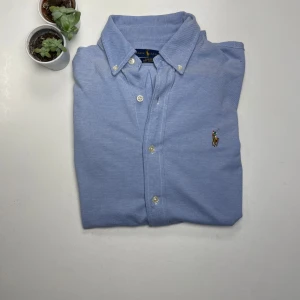 Ralph Lauren Skjorta  - Snygg blå skjorta från Ralph Lauren i S. Skjortan har en klassisk krage med knappar och är broderad med den ikoniska logotypen på bröstet. Perfekt för en sommar dag på stranden eller en lugn kväll! 🌴🥥Skjortan är i underbart skick. PM för frågor! 