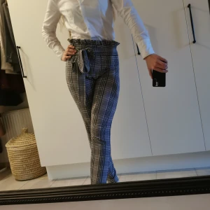 Rutig byxa med knytband - Snygga högmidjade byxor med svartvitt rutmönster och knytband i midjan från shein. Byxorna har en tight passform och är perfekta för en stilren look. De har en volangdetalj vid midjan som ger en extra touch. Storlek 40, men passar även 38. Längd: 105cm.
