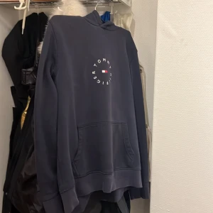 Mörkblå hoodie från Tommy Hilfiger - Säljer en snygg mörkblå hoodie från Tommy Hilfiger med deras ikoniska logga framtill. Tröjan har en klassisk känguruficka och en bekväm huva. Perfekt för en avslappnad stil.