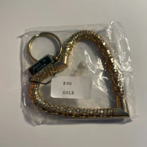 Guld hjärtformat nyckelring - Elegant hjärtformad nyckelring i guld med en flätad design. Perfekt som en stilfull accessoar för dina nycklar eller för din väska. Andvända tyvärr inte för jag är silver!