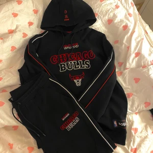 Svart hoodie från Boss med Chicago Bulls-tryck - Snygg svart hoodie från Boss med Chicago Bulls-tryck i rött och vitt. Hoodien har en klassisk design med en stor logga på framsidan och detaljer i rött längs ärmarna. Perfekt för basketfans! 🏀