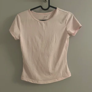 Ljusrosa kortärmad topp - Säljer en ljusrosa kortärmad topp med rund halsringning. Toppen har en tight passform och är perfekt för en stilren look. Enkel och snygg att matcha med jeans eller kjol.