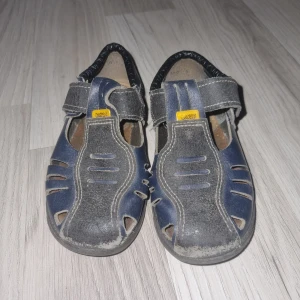 Blå sandaler med kardborreband - Säljer ett par blå sandaler med praktiska kardborreband för enkel justering. Skorna har en robust sula och flera utskärningar för ventilation. Perfekta för sommarens äventyr. Kavat I storlek 25.