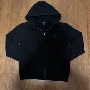 Svart Ralph Lauren hoodie med dragkedja - Svart Ralph Lauren hoodie med dragkedja, röd ponnylogga.  🌟Riktigt fint skick, endast använd ett par gånger. Lite smutsig men försvinner med en tvätt.  🐑100% bomull, riktigt bekvämt och stretchigt material.  📬Jag skickar inom samma eller nästa dag efter köpet.  📏Storlek L (14-16) för barn, men passar XS/S i vuxenstorlek också. Se mått nedan.  📐43cm axelbredd, 56cm full längd, 50cm ärmlängd (alla mätt på plan mark)  😊 Ställ gärna frågor.  #ralphlauren #poloralphlauren #zip #zipup #tröja  #vit 