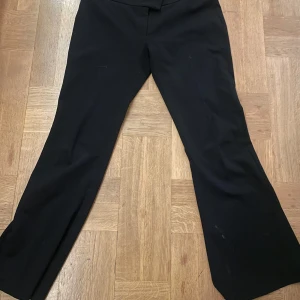 Svarta kostymbyxor från Gina Tricot - Snygga svarta kostymbyxor från Gina Tricot i storlek L och även M. Byxorna har en klassisk bootcut-stil och är försedda med dragkedja och hyska för en säker passform. Perfekta för en stilren look.