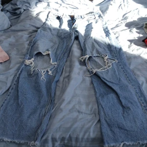 Blå jeansbyxor från &Denim - Säljer ett par blå jeansbyxor från &Denim med en ultra hög midja och wide fit. Byxorna har stora slitningar på knäna för en trendig look. Perfekta för dig som gillar en avslappnad stil.