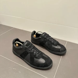 GATS Sneakers - Svart GATS som ser exakt likadant ut som Maison Marigela! Skorna är i bra skick men mockan är lite smutsig och slitten, går säkert att fixa med ett mocka kit men det har jag tyvärr inte :/ Underdelen av skorna sitter lite löst men det ser man bara ifall man försöker dra isär dem, annars sitter dem tätt och bra! Mycket bra skor ifall du vill ha något som ser ut som Maison Margielas! Storlek: 43 