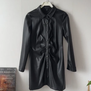 Skinn klänning  - Snygg svart klänning med knappar framtill. Den har en klassisk krage och långa ärmar, perfekt för en stilren look. Klänningen har en figurnära passform och är i storlek EU 38. Använd en två gånger, pris kan alltid diskuteras 🌸🌸