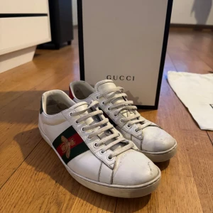 Gucci Ace  - Snygga vita sneakers från Gucci med klassiska gröna och röda ränder samt ett broderat bi på sidan. Skorna har snörning och en bekväm sula med mönster. Perfekta för en stilren look. Nypris 8000kr mitt pris 2499.  Pris kan diskuteras vid snabb affär 