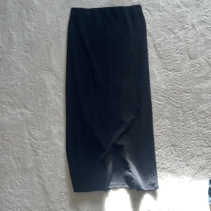 Svart långkjol - Elegant svart långkjol med en stilren design. Kjolen har en diskret slits baktill som ger extra rörelsefrihet. Perfekt för en chic och minimalistisk look.