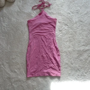 Rosa axelbandslös klänning - Snygg rosa axelbandslös klänning i en tight passform. Perfekt för sommarens varma dagar. Klänningen har en enkel design med knytband runt halsen.
