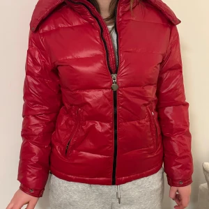 Röd dunjacka - Snygg röd dunjacka med dragkedja och luva. Liknar lite monkler maya. Den är ialafall en perfekt röd och jackan är supersnygg men kommer ej till använd. Använd fåtal gånger.