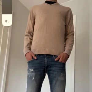 Beige tröja från Tommy Hilfiger - Säljer en snygg beige tröja från Tommy Hilfiger. Den är i en mjuk och skön blandning av bomull och kashmir, perfekt för både höst och vår. Tröjan har en v-ringad design och långa ärmar, vilket gör den både stilren och bekväm. Passar perfekt till ett par jeans för en avslappnad look.