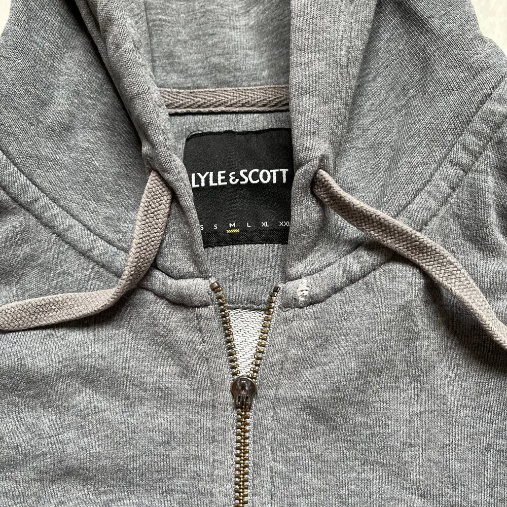 Säljer en snygg grå hoodie från Lyle & Scott. Den har en dragkedja framtill och en broderad gul logga på bröstet. Perfekt för en avslappnad stil och passar till alla tillfällen. Den är i okej skick och superbekväm! Är 180 och väger 75kg. Tröjor & Koftor.