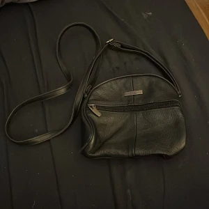 Svart axelväska i skinn - Säljer en stilren svart axelväska i skinn. Den har en praktisk dragkedja framtill och en justerbar axelrem. Perfekt för vardagsbruk eller en kväll ute. 🖤