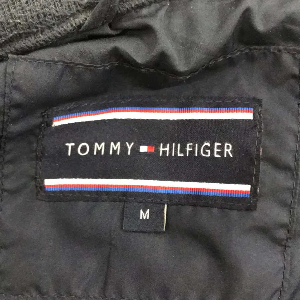 Säljer en snygg mörkblå jacka från Tommy Hilfiger. Den har en stilren design med knappar framtill och en hög krage. Jackan är quiltad och har praktiska fickor med knappar på bröstet samt en dragkedja på ena sidan. Perfekt för höst och vår!. Jackor.