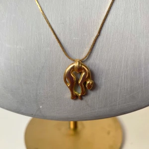 Guldhalsband och örhängen med abstrakt design - Säljer ett elegant set med ett guldhalsband och matchande örhängen. Halsbandet har en tunn kedja med ett hängsmycke med panter. Örhängena har samma unika form och ger en stilren look.  Kedjan bytes mot annan kedja vid köp.