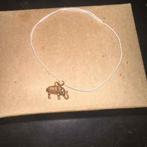 Armband med elefantberlock - Säljer ett enkelt och stilrent armband med en söt elefantberlock i guld. Kedjan är tunn och vit, vilket ger en fin kontrast till den gyllene berlocken. Perfekt för att lägga till en unik touch till din outfit!