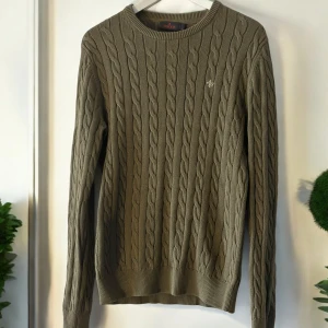 Olivgrön stickad tröja från Morris - Olivgrön stickad tröja från Morris. Den har ett klassiskt flätmönster och har ribbade muddar vid ärmslut och nederkant. Tröjan är använd vid ytterst få tillfällen och därav i mycket bra skick. Storlek S.