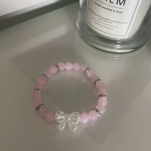 Rosa pärlarmband med rosett - Säljer ett supergulligt rosa pärlarmband med en söt rosett i mitten. Armbandet har små silverfärgade detaljer mellan pärlorna som ger det en extra touch av elegans. Perfekt för att piffa upp vilken outfit som helst! 💖