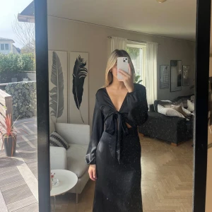 Svart satinklänning  - Säljer denna svarta satinklänningen med knytdetalj vid brösten. Använd en gång så i väldigt fint skick. St S🤩🙌🏼