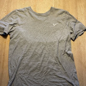 Grå t-shirt från Nike - Säljer en grå t-shirt från Nike i storlek M. Den är i bra skick och perfekt för träning eller vardagsbruk. T-shirten har en normal passform och är kortärmad med en liten Nike-logga på bröstet. Materialet känns mjukt och bekvämt.
