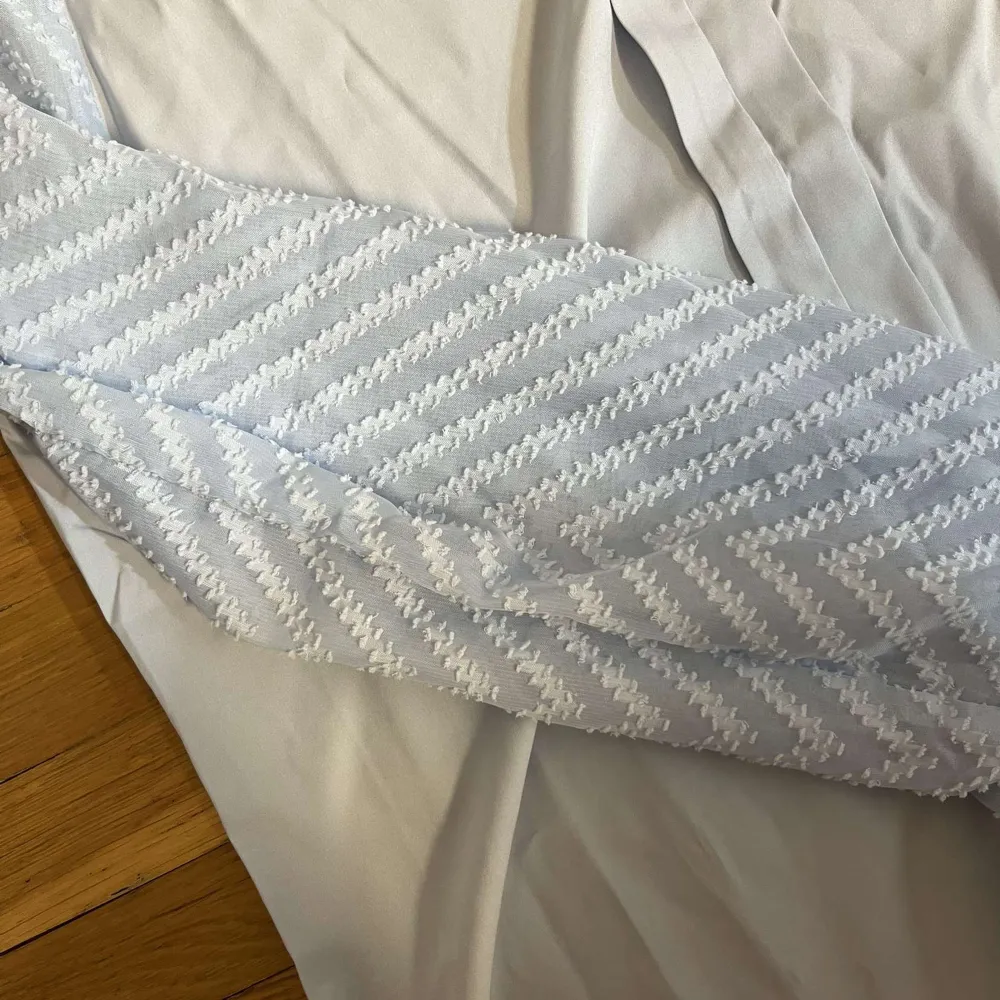 Säljer en stilren vit blus med unika mönstrade ärmar i ljusblått och vitt. Blusen har en v-ringad design och den har långa ärmar med ett snyggt zigzag-mönster, den är i storlek L men sitter som M, den är helt ny utan defekter. Puserot.