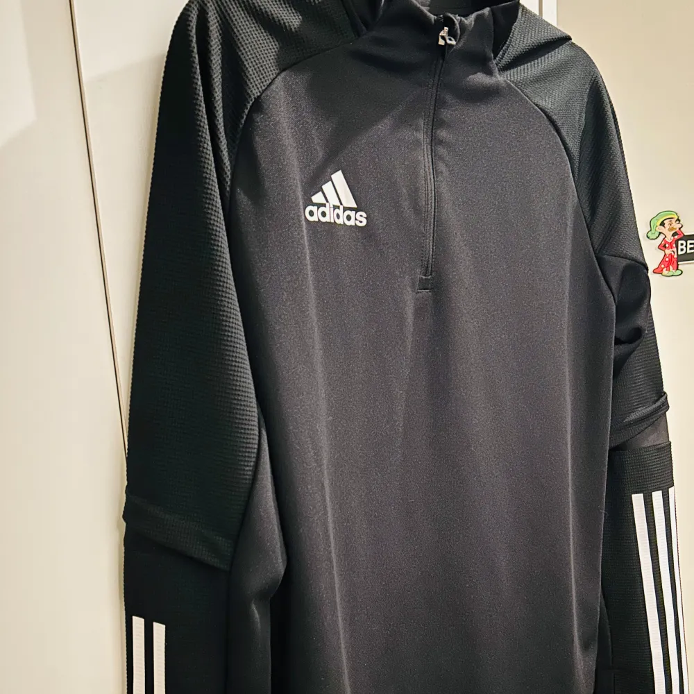 Säljer en snygg och sportig svart långärmad tröja från Adidas. Den har en halv dragkedja framtill och de klassiska tre ränderna på ärmarna. Perfekt för träning eller en avslappnad dag. Materialet är AEROREADY, vilket gör den bekväm och andas bra. . Tröjor & Koftor.