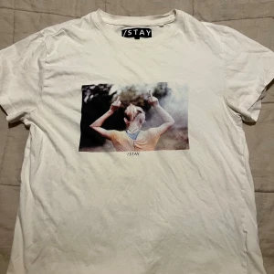Vit t-shirt från STAY - Säljer en vit t-shirt från STAY i storlek S. Den har ett coolt tryck på framsidan med en person som håller upp fingrarna över huvudet. Perfekt för en avslappnad stil och passar bra till jeans. T-shirten är i bra skick och superbekväm att ha på sig.