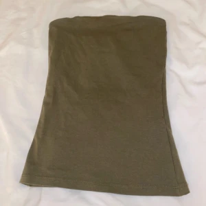 Olivgrön tubtopp - Säljer en enkel och stilren olivgrön tubtopp. Perfekt för sommardagar eller att ha under en kavaj. Toppen är i ett mjukt och stretchigt material som sitter bekvämt på kroppen. 