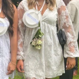 Vit spetsklänning med långärmad design - Säljer en superfin vit klänning i spets med långärmade detaljer. Den har en v-ringad design och är perfekt för sommarens alla fester. Klänningen är kort och har en romantisk känsla med sina blommiga spetsmönster. Perfekt för student eller midsommar!