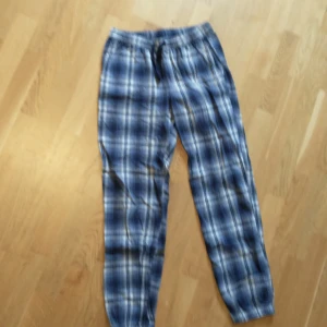 Rutig byxa från KappAhl - Säljer ett par bekväma och stiliga rutiga byxor från KappAhl. De är i en snygg blå och vit färgkombination med elastisk midja och snörning för extra komfort. Perfekta för en avslappnad dag hemma eller en chill dag ute. Passar bra till både t-shirt och hoodie!Hör av dig om frågor!💕