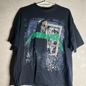 Mörkblå Metallica t-shirt - Cool mörkblå t-shirt med Metallica-tryck i grönt och ett skelettmotiv. Perfekt för rockälskare som vill ha en unik stil. T-shirten har en oversized passform. OBS den är croppad längst ned