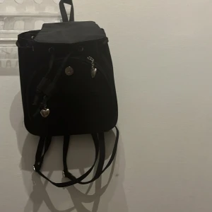Svart ryggsäck med hjärtformade detaljer - Snygg svart ryggsäck med hjärtformade dragkedjor och justerbara axelremmar. Perfekt för att bära dina dagliga nödvändigheter. Rymligt huvudfack med extra innerfickor för bättre organisering.Finns inga lappar på.Hyfsat bra skick