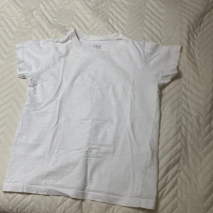Vit t-shirt från 157 - Säljer en klassisk vit t-shirt från 157 i 100% bomull. Perfekt basplagg med korta ärmar och rund hals. Enkel och stilren design som passar till det mesta.