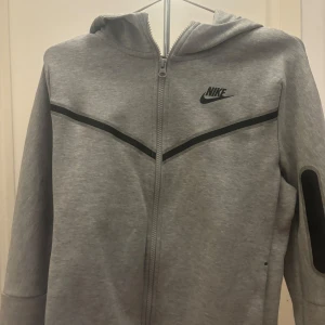  Nike - Säljer en grå hoodie från Nike med dragkedja och svart logotyp på bröstet. Storlek 170 men passar mig som brukar ha xs - s i kläder. Använd 2 gånger, skick 10/10