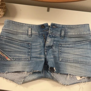 Super snygga låga blå jeansshorts från Diesel - Kan gå ner i pris. Snygga blå jeansshorts från Diesel med råa kanter och coola detaljer som nitar på bakfickan. Shortsen har en låg midja. Säljer för att de är för små. Köpte som skinny jeans men klippte till shorts. Aldrig andvända. Väldigt bra skick. Storlek 27 men skulle säga att de är ganska små i storleken med tanke på att jag brukar ha 25 i andra jeans. Har dock aldrig provat disel jeans så kan stämma med diesels storlekar.