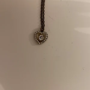 Halsband med hjärtformad berlock - Snyggt halsband med en hjärtformad berlock dekorerad med glittrande stenar. Perfekt för att ge en touch av elegans till din outfit.