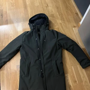 Svart parkajacka från Didriksons - Snygg svart parkajacka från Didriksons med quiltad insida och praktisk huva. Jackan har dragkedja och knappar framtill för extra skydd mot väder och vind. Perfekt för kyliga dagar. Jackan är storlek M och har använd den ca 4 gånger sedan jag köpte den, köpte den för 4000kr ny på volt ocv säljer endast för 2500!