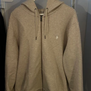 Beige hoodie från Polo Ralph Lauren - Säljer en beige hoodie från Polo Ralph Lauren med dragkedja och justerbar huva. Endast testad och knappt använd, nyskick.
