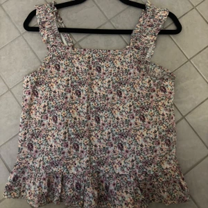 Färgglad blommig linneblus från Name it - Säljer en blommig jätte gullig linneblus från märket name it. Storleken är 146-152 11-12yr. SKRIV INNAN KÖP💞 OCH GE GÄRNA PRISFÖRSLAG. Den har en skön och fin passform och resår i ärmarna. Längst ner har den en jättefin volang. Linneblus en har ett blommigt mönster i flera färger orange, lila , grön. Passar perfekt till sommaren.